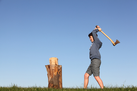 Young boy outdoors chopping wood with blue skyの写真素材