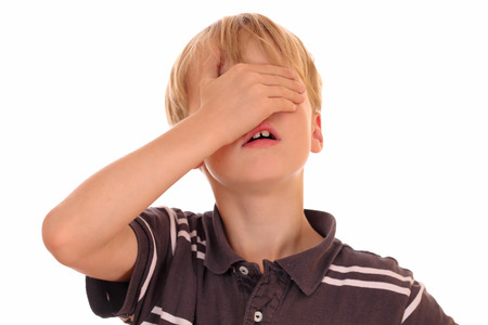 Portrait of a young boy covering his eyes on white backgroundの写真素材