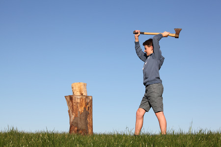 Young boy outdoors chopping wood with blue skyの写真素材