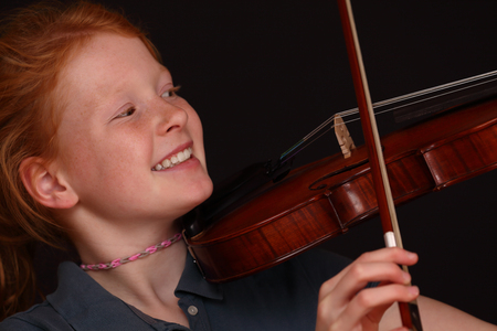 Portrait of a young girl playing violin on black backgroundの写真素材