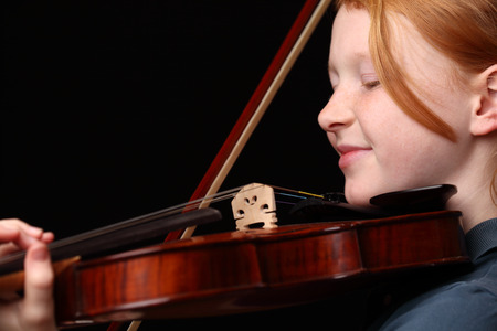 Portrait of a young girl playing violin on black backgroundの写真素材