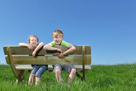 Two happy young kids sitting on a bench in summerの写真素材