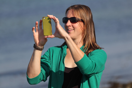 Portrait of a beautiful woman taking a picture with her smartphone at the beachの写真素材
