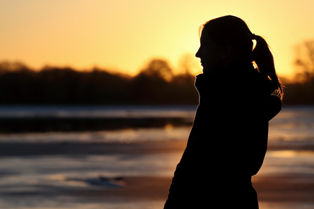 Silhouette of a woman at lake at sunsetの写真素材