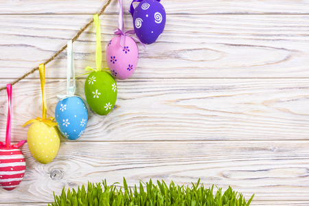 Colorful easter eggs hanging on rustic wooden background and green fresh grass with space. easter...