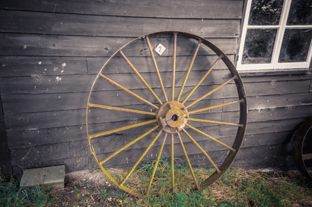 ancient metal wheel standing near wooden wallの写真素材