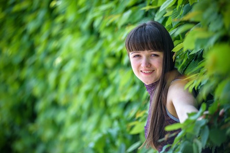 beautiful smiling girl looking at you against spring green blurred background. playing with her hair.の写真素材