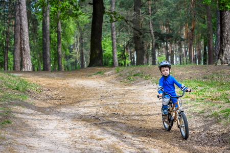 Happy cute blond kid boy having fun his first bike on sunny summer day, outdoors. Happy child making sports. Active leisure for children.Kid boy wear safety helmet. boy is smiling and cicling.の写真素材