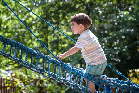 Little climber takes the rope bridge. Boy has fun time, kid climbing on sunny warm summer day.の写真素材