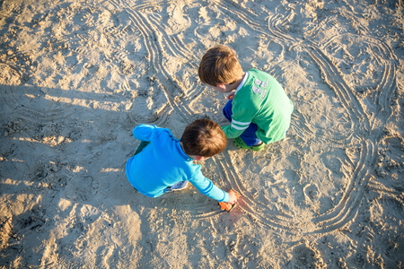 Two happy caucasian kids, brothers, playing together with toy cars sitting outdoors at pebble beach against the sea beachの写真素材