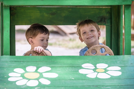 Two little brother toddlers playing with toy car in summer garden. Boys having fun and good time. In wooden toy car at playground.の写真素材