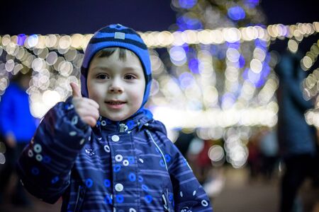 family, childhood, season and people concept - happy kid boy in winter clothes over snow city...