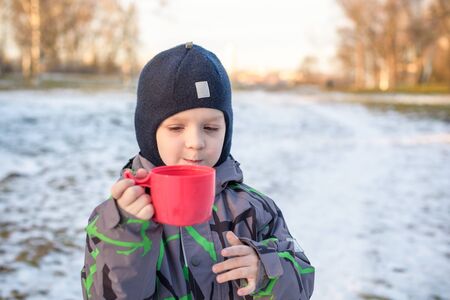 Little cute kid boy with cup of steaming hot chocolate or children punch. Happy child play in winter forest outdoors.の写真素材