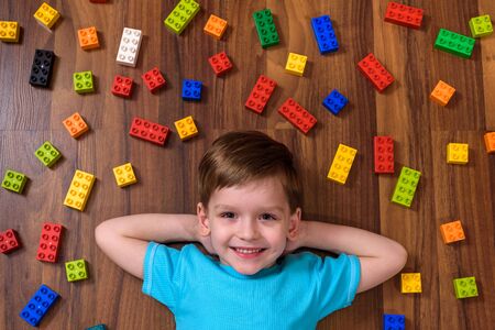 Little caucasian child playing with lots of colorful plastic blocks indoor. Kid boy wearing colorful shirt and having fun with building and creating.の写真素材