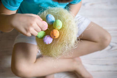 Cute little boy holding a nest with colored Easter eggs at home on Easter day. Celebrating Easter at...