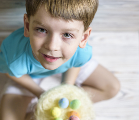 Cute little boy holding a nest with colored Easter eggs at home on Easter day. Celebrating Easter at...