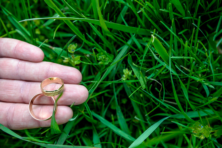 wedding rings on grooms hand on green grass backgroundの写真素材