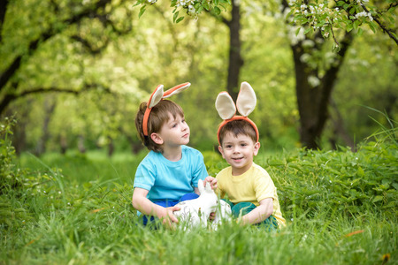 Two little kids boys and friends in Easter bunny ears during traditional egg hunt in spring garden, outdoors. Siblings having fun with finding colorful eggs. Old christian and catholoc tradition.の写真素材