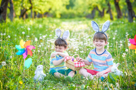 Two boys in the park, having fun with colored eggs for Easter. Traditional egg hunt morning. Religious holiday concept.の写真素材