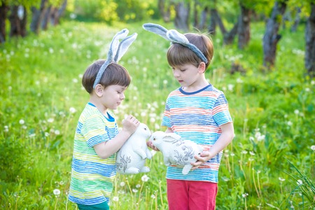 Two little kids boys and friends in Easter bunny ears during traditional egg hunt in spring garden, outdoors.の写真素材