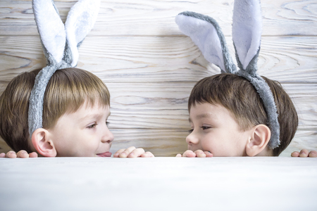 Two cute little brothers wearing bunny ears playing egg hunt on Easter. Adorable children celebrate Easter at homeの写真素材