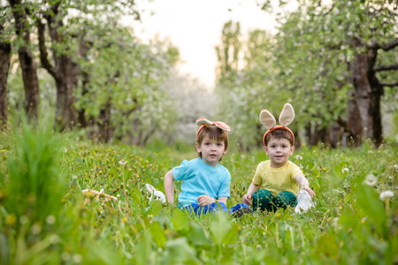 Two little kids boys and friends in Easter bunny ears during traditional egg hunt in spring garden, outdoors.の写真素材