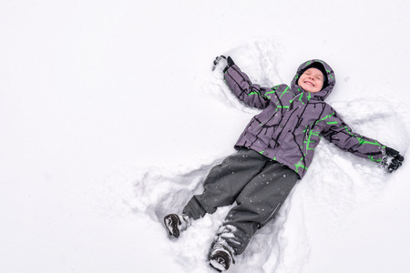 Cute little kid boy in colorful winter clothes making snow angel, laying down on snow. Active outdoors leisure with children in winter. Happy childの写真素材