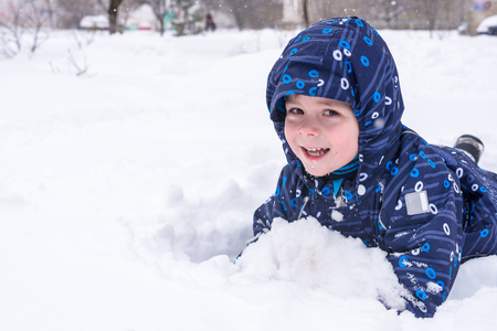 a little child looks out of the snow or pieces of ice. A child plays with snow. lay down in snow. smiling happy kidの写真素材