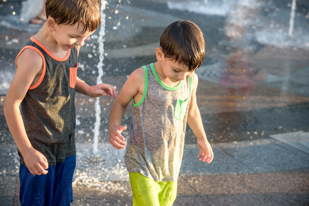 Happy kids have fun playing in city water fountain on hot summer day. Boys happy and smiling brother best friends. Ecology concept.の写真素材