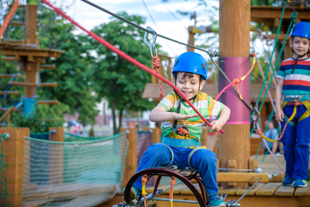 Little cute boy enjoying activity in a climbing adventure park on a summer sunny day. toddler climbing in a rope playground structure. Safe Climbing extreme sport with helmet and Carabiner. insuranceの写真素材