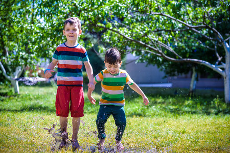 Little boy and his brother play in summer park. Children with colorful clothes jump in puddle and mud in the garden. Kids walk in summer puddle after shower. Outdoor fun by any weather.の写真素材