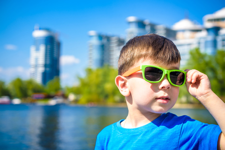 Portrait of a cute little boy with a sunglasses, sitting by the river - the lake and enjoy the beautiful and sunny day.の写真素材