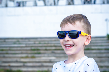 Scared surprised astonished mixed Caucasian male child with sunglasses, poses against brick white wall background. White excited kid models outdoors.の写真素材