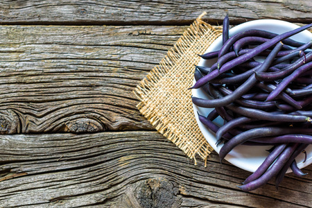 purple string beans on a wooden plate on a wooden background.