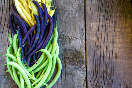 Collection of green, yellow and purple bush beans, opened green peas on wooden rustic background.