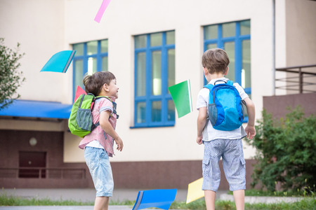 Happy children - two boys friends with books and backpacks on the first or last school day. Schoolchildren celebrating end of term. Students to complete academic year. Full length outdoor portrait.の写真素材
