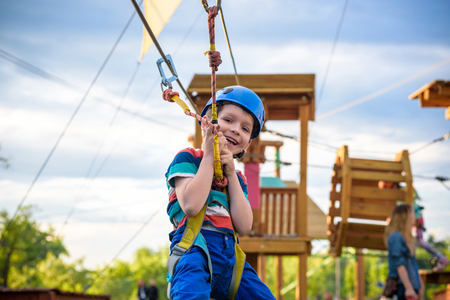 Little cute boy enjoying activity in a climbing adventure park on a summer sunny day. toddler climbing in a rope playground structure. Safe Climbing extreme sport with helmet and Carabiner. insuranceの写真素材