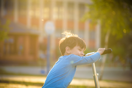 Little toddler boy riding and his scooter in summer warm evening park.の写真素材
