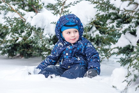 Winter portrait of kid boy in colorful clothes, outdoors during snowfall. Active outdoors leisure with children in winter on cold snowy days. Happy child having fun with snowの写真素材
