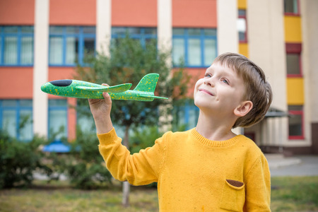 Happy kid playing with toy airplane against nice building background. Boy throw foam plane in School or kindergarten field. Best childhood concept.の写真素材