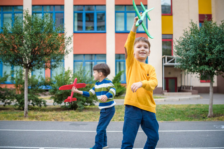 Happy two brother kids playing with toy airplane against blue summer sky background. Boys throw foam plane in city. Best childhood concept.の写真素材