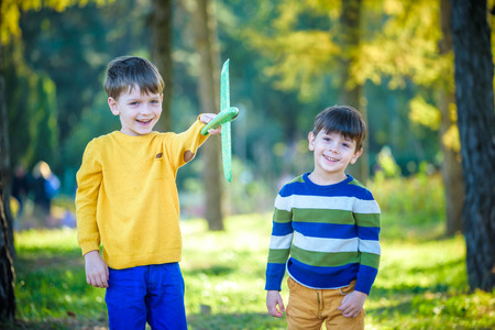 Happy two brother kids playing with toy airplane against blue summer sky background. Boys throw foam plane in the forest or park. Best childhood concept.の写真素材