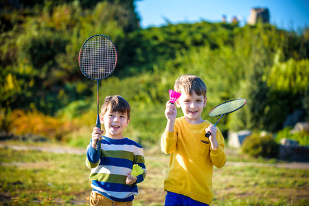 Two active preschool boy playing badminton in outdoor court in summer. Kids play tennis. School sports for children. Racquet and shuttlecock sport for child athlete. Friends happy together warm field.の写真素材