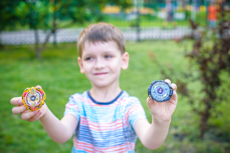 Boy playing with modern spin top outdoors. Entertainment game for children. Top, triggered by a trigger. Kid demonstrate two different variants choosing which is better.の写真素材