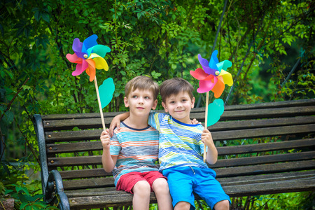 Portrait of two boys, sibling brothers and best friends smiling. Kids sitting on bench play together with pinwheel. Outdoors leisure friendship family concept.の写真素材