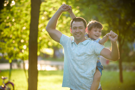 Father and son hugging and playing together in green nature on warm sunny summer evening. Concept of friendship between children and parents, happy family.の写真素材