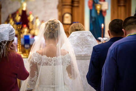 Bride and groom stand with crowns during the ceremony in church.の写真素材