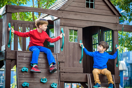 Two little boys playing together and having fun. Lifestyle family moment of siblings on playground. Kids friends play on tree house climbing on rope or stairs.の写真素材