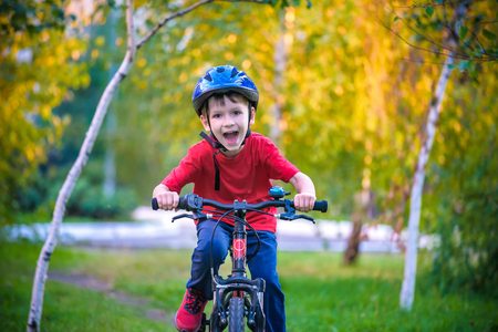 Happy kid boy of 6 years having fun in autumn forest with a bicycle on beautiful fall day. Active child making sports. Safety, sports, leisure with kids concept.の写真素材