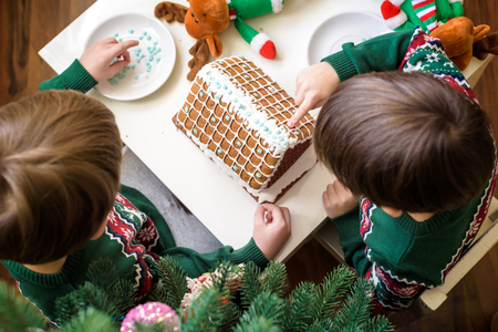 Two sweet boys, brothers, making gingerbread cookies house, decorating at home in front of the Christmas tree, child playing and enjoying, Christmas concept.の写真素材